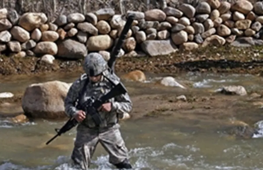 Chris Spositi crossing a rocky river on foot patrol, rifle in hand